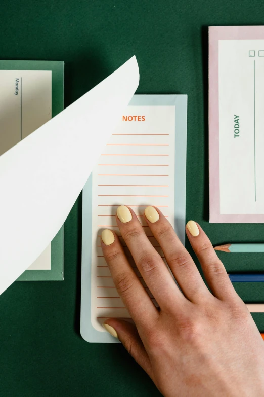 a close up of a person writing on a notepad, by Anita Malfatti, diecut, green and orange theme, sleek hands, pastelle colors