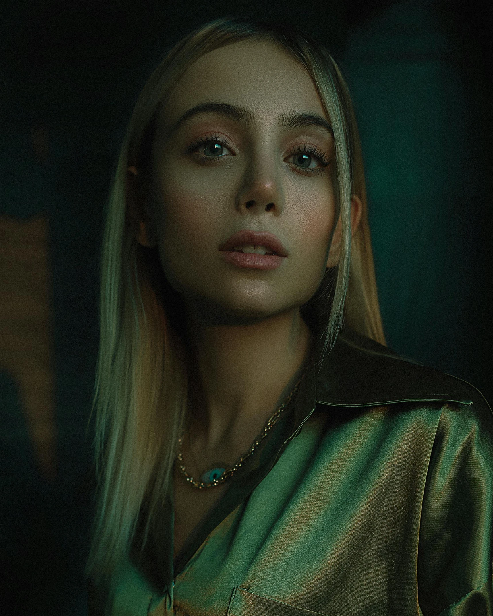 a woman with long blonde hair standing in a dark room, a colorized photo, inspired by Elsa Bleda, trending on pexels, hyperrealism, wearing green jacket, zoe kazan, cyber necklace, portrait of vanessa morgan