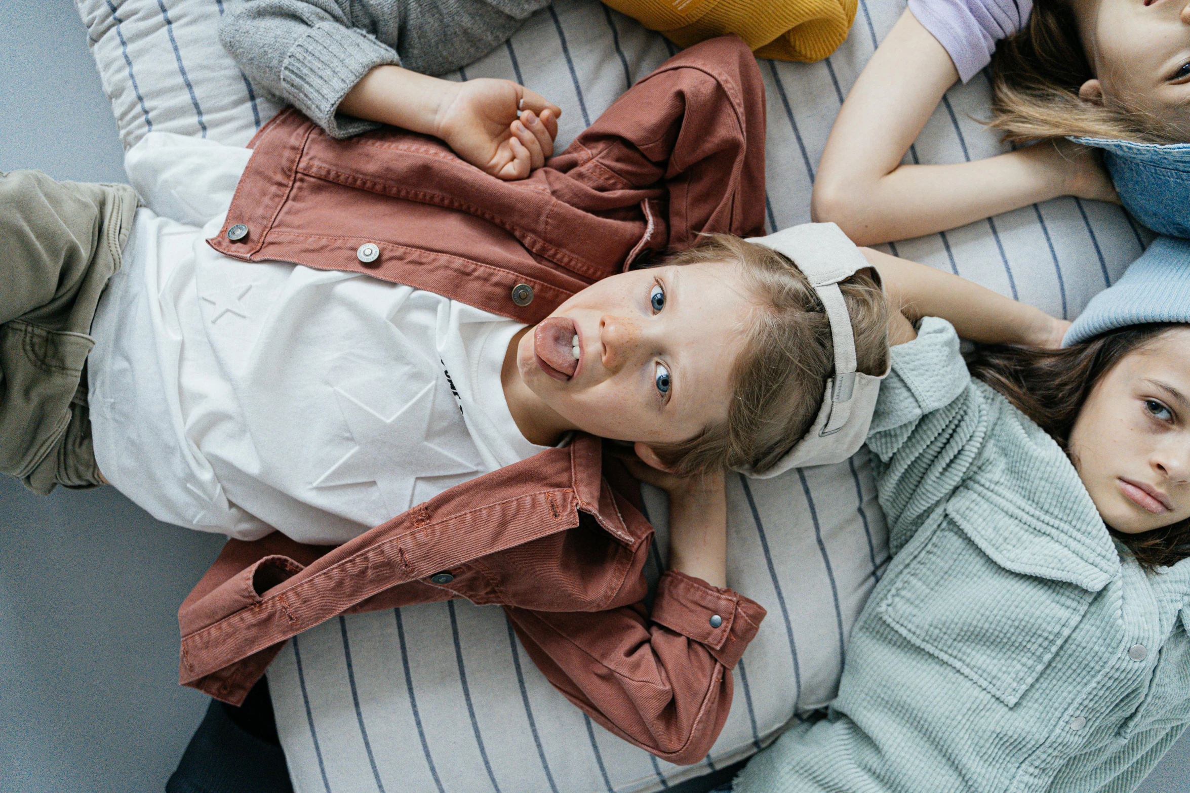 a group of children laying on top of a bed, by Emma Andijewska, trending on pexels, wearing a jeans jackets, caring fatherly wide forehead, girl with brown hair, top angle