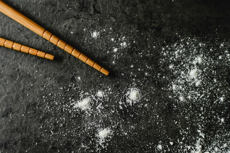 a pair of chopsticks sitting on top of a table, an album cover, trending on pexels, visual art, flour dust, cinnamon, with a black background, baking cookies