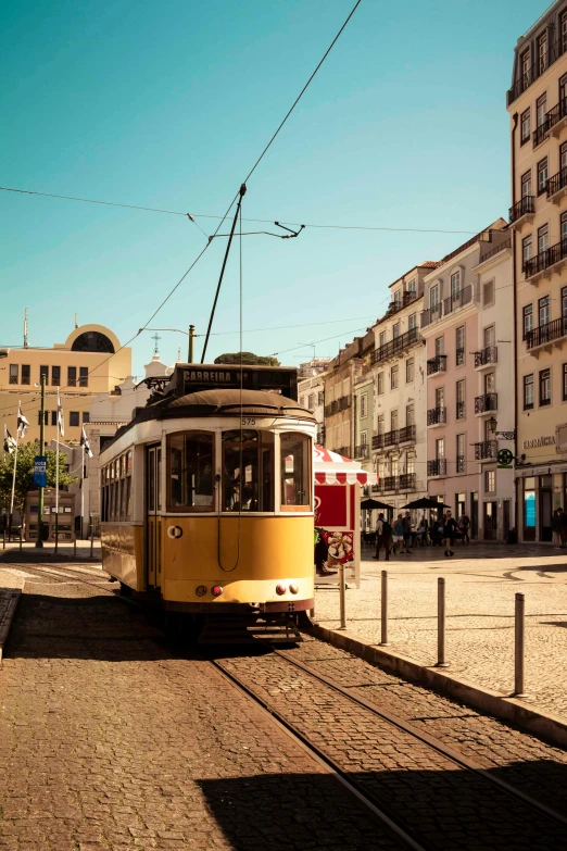 a yellow trolley traveling down a street next to tall buildings, inspired by Almada Negreiros, renaissance, bathed in golden light, round buildings in background, ignant, trams