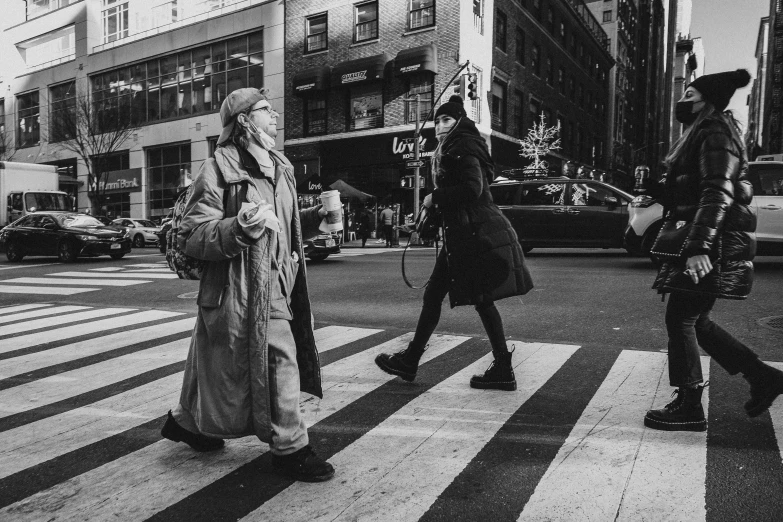 a couple of people that are walking across a street, a black and white photo, he wears a big coat, crosswalks, concrete jungle, old woman