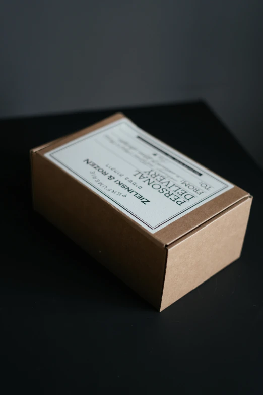 a brown box sitting on top of a table, a picture, product label, white font on black canvas, dark. no text, small manufacture