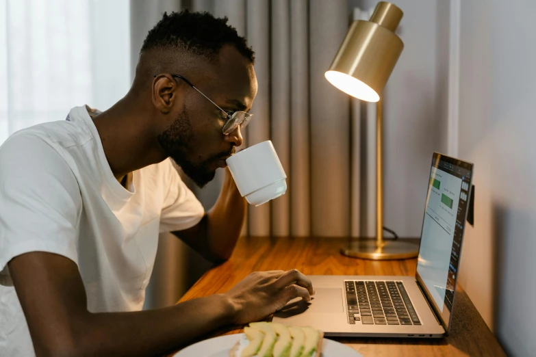 a man sitting at a table with a laptop and a cup of coffee, a screenshot, pexels contest winner, happening, man is with black skin, sleepy, lights off, profile image