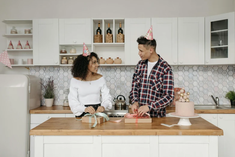 a man standing next to a woman in a kitchen, pexels contest winner, happening, birthday wrapped presents, background image, curls on top, party hats