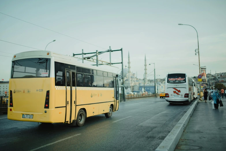 a yellow bus driving down a street next to a white bus, pexels contest winner, hurufiyya, turkish and russian, grey, islamic, ismail inceoglu and ruan jia