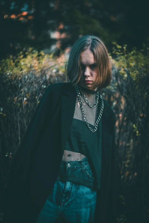 a woman standing in front of a wooden fence, an album cover, inspired by Elsa Bleda, trending on pexels, aestheticism, metal chain and black cape, portrait androgynous girl, wearing a black jacket, ((chains))