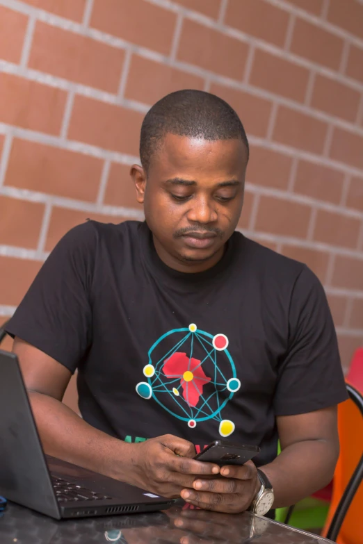 a man sitting at a table using a cell phone, by Chinwe Chukwuogo-Roy, he is wearing a black t-shirt, programming, 2 5 6 x 2 5 6 pixels, starry