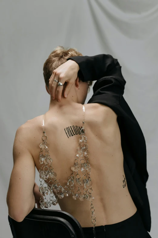 a woman sitting in a chair with a tattoo on her back, inspired by Nikolaj Abraham Abildgaard, trending on pexels, made of crystals, cai xukun, bralette, androgynous male