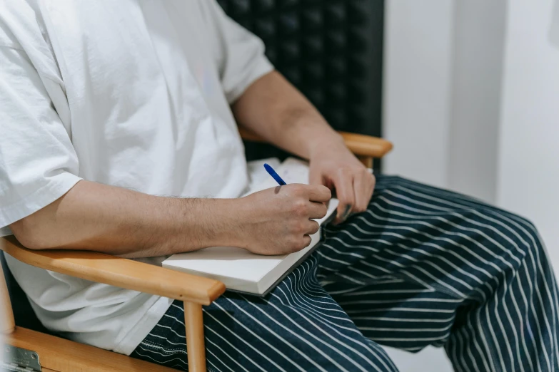 a man sits in a chair writing on a notepad