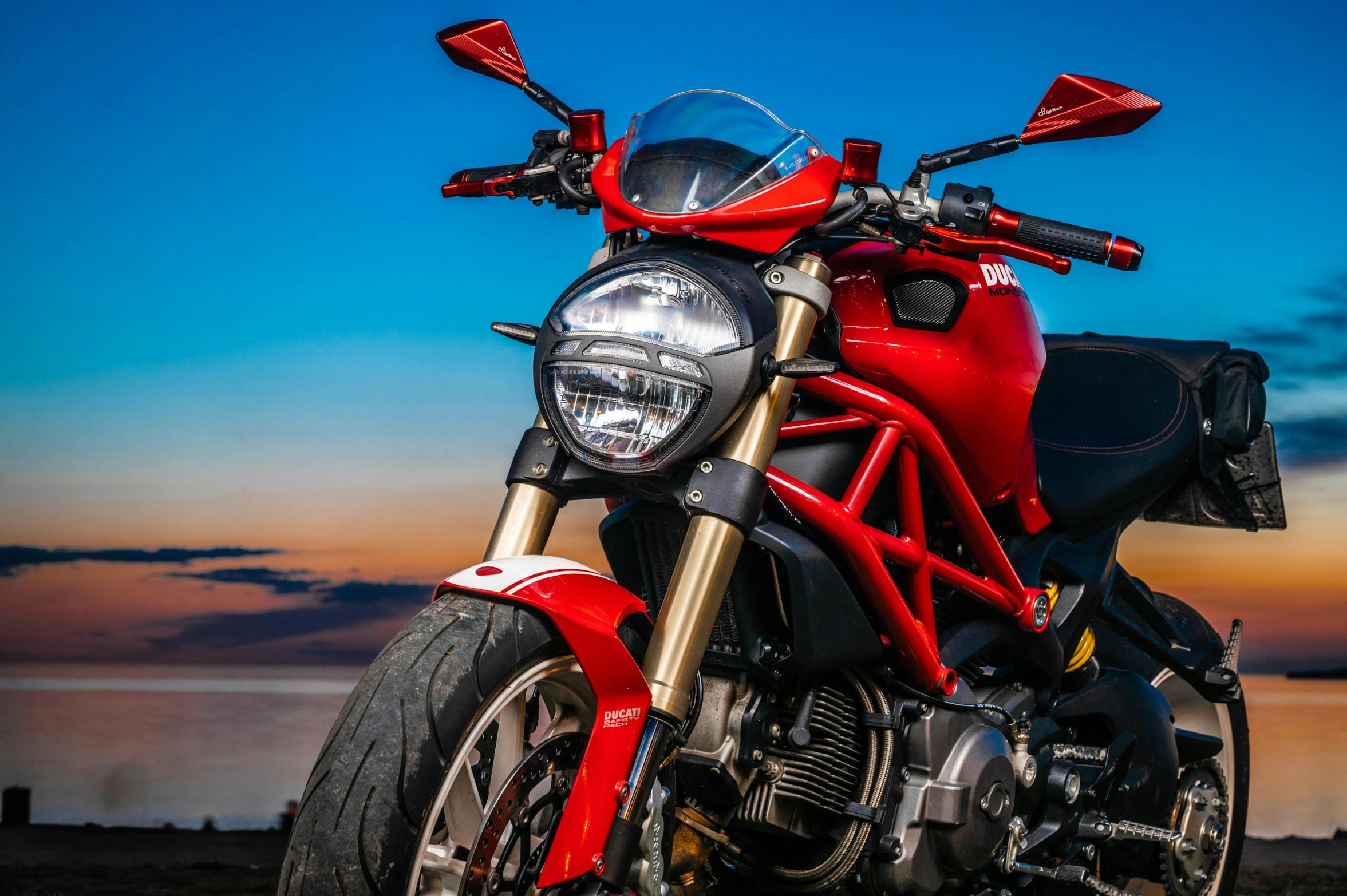 a red motorcycle parked next to a body of water, pexels contest winner, photorealism, devil's horns, evening lighting, perfect crisp sunlight, avatar image