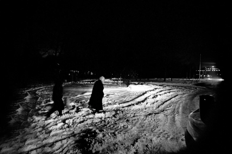 a couple of people that are standing in the snow, a black and white photo, land art, moonlit parking lot, local people chasing to attack, cloaked dark night, distant glowing figures