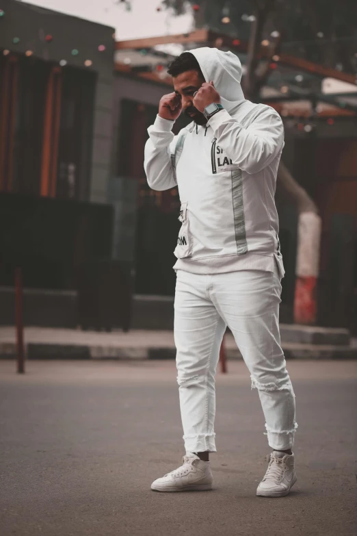 a man standing on a street talking on a cell phone, inspired by Amir Zand, pexels contest winner, white adidas pants, wearing a track suit, white metallic armor, frontal pose