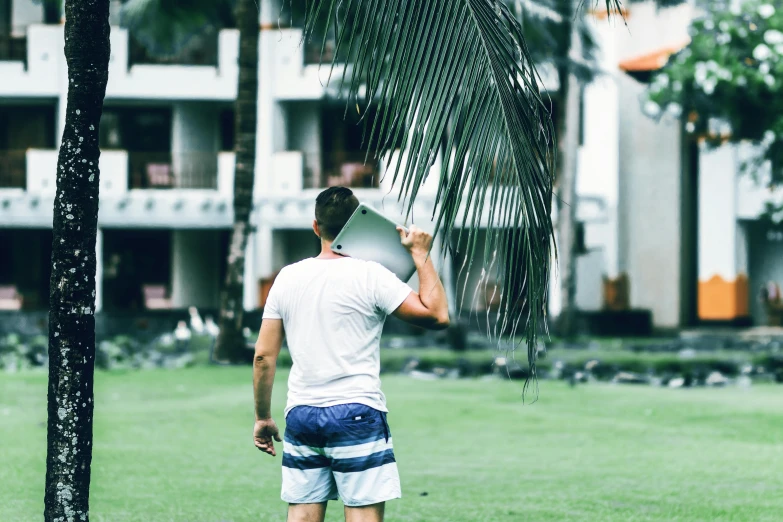 a man standing on top of a lush green field, palm leaves on the beach, college, profile image, carrying a tray