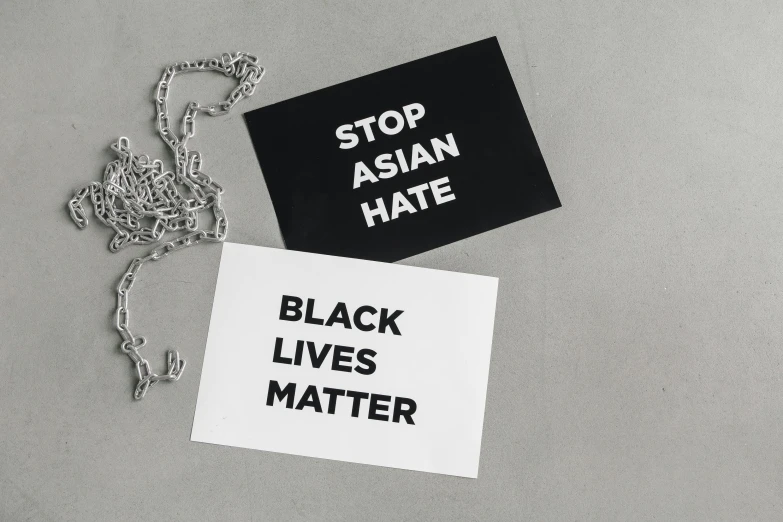 a sign that says stop asian hate and black lives matter, a black and white photo, private press, pair of keycards on table, outlive streetwear collection, choker, postcard