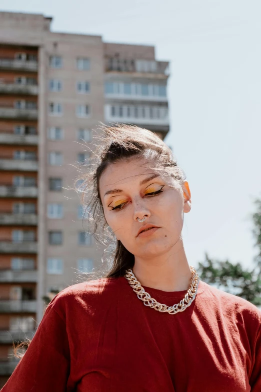 a woman standing in front of a tall building, an album cover, trending on pexels, ukrainian girl, wearing gold detailed choker, wearing red and yellow clothes, view from the street