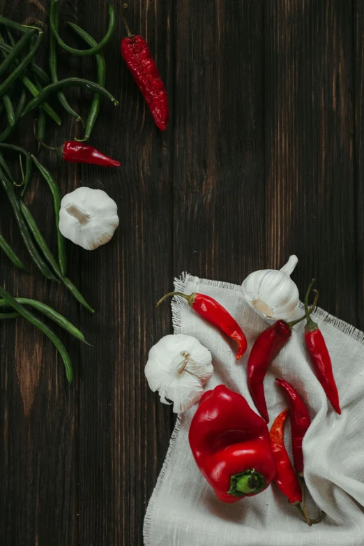 a bunch of red peppers sitting on top of a white cloth, a still life, by Julia Pishtar, pexels contest winner, renaissance, garlic on background, on a wooden desk, square, dark backdrop