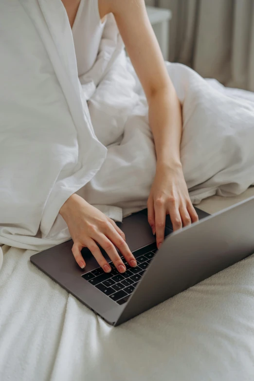 a woman sitting on a bed using a laptop computer, pexels, curled up under the covers, sleek hands, tech robes, wearing a white button up shirt