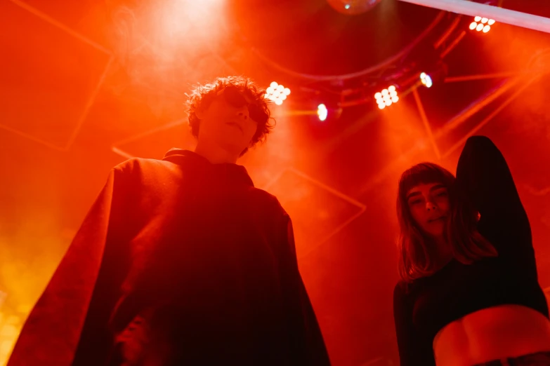 a couple of people standing on top of a stage, pexels contest winner, antipodeans, red glow, declan mckenna, at a rave, looking from slightly below