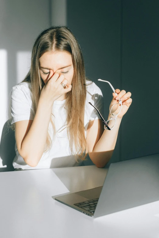 a woman sitting at a table in front of a laptop, we're all very tired, blinding sun, woman crying, a very macular woman in white