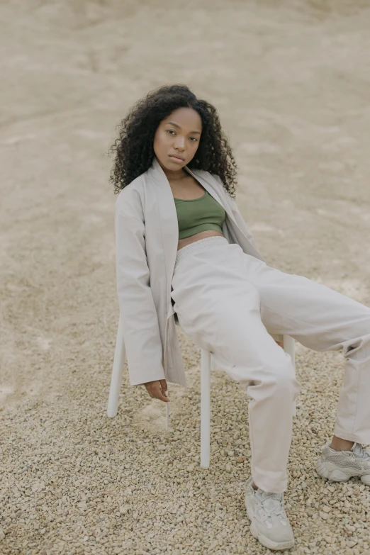 a woman sitting on a chair in the sand, trending on unsplash, renaissance, wearing a track suit, muted green, an all white human, wearing a crop top