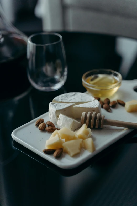 a white plate topped with cheese and nuts next to a glass of wine, honey, premium, ritual, black & white