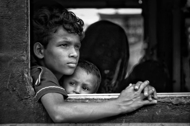 a black and white photo of two children looking out of a window, by Sudip Roy, flickr, square, caravan, beautiful man, crowded