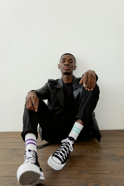 a man sitting on the floor with his feet up, by Nina Hamnett, playboi carti portrait, sitting with wrists together, very tall, on a pale background