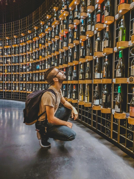 a man crouched down looking at the wine shelves