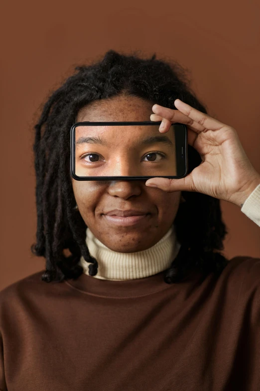 a woman holding a cell phone up to her face, a picture, trending on pexels, afrofuturism, small square glasses, boy with neutral face, centered in a frame, concept photo