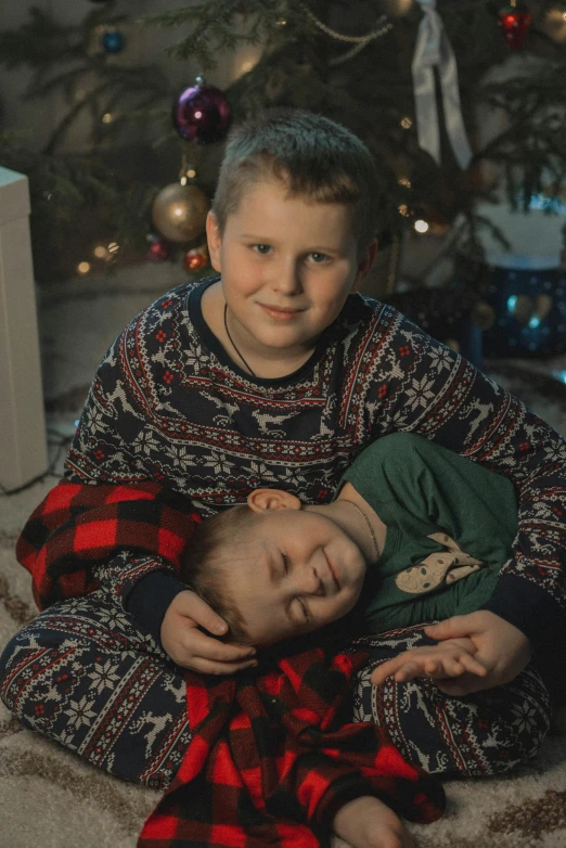 a little  holding a baby with a christmas tree in the background