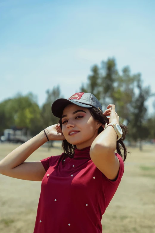 a woman standing in a field holding a baseball bat, by Robbie Trevino, instagram, wearing a red backwards cap, golf course, wears a light grey crown, beautiful mexican woman