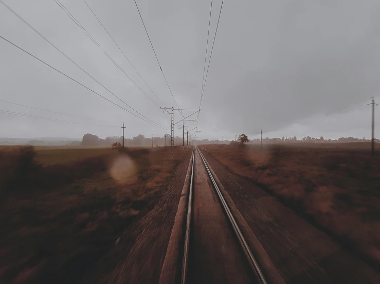 a train traveling down train tracks next to power lines, an album cover, by Lucia Peka, unsplash contest winner, realism, under a gray foggy sky, first-person pov, instagram post 4k, rural dystopian