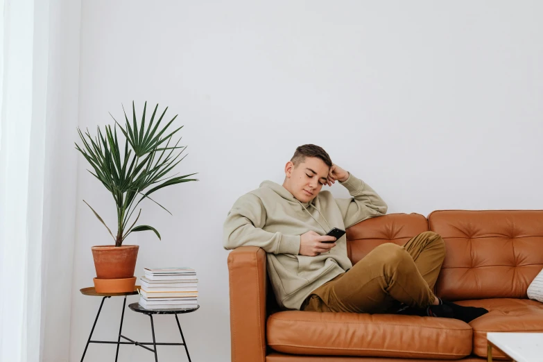 a man sitting on top of a couch next to a plant, trending on pexels, happening, he is wearing a brown sweater, male teenager, slightly tanned, fatigue