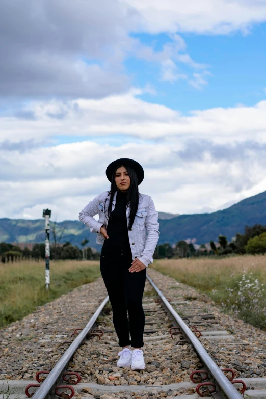 a woman standing on a train track with mountains in the background, by Lucia Peka, white hijab, black pointed hat, wearing farm clothes, alanis guillen