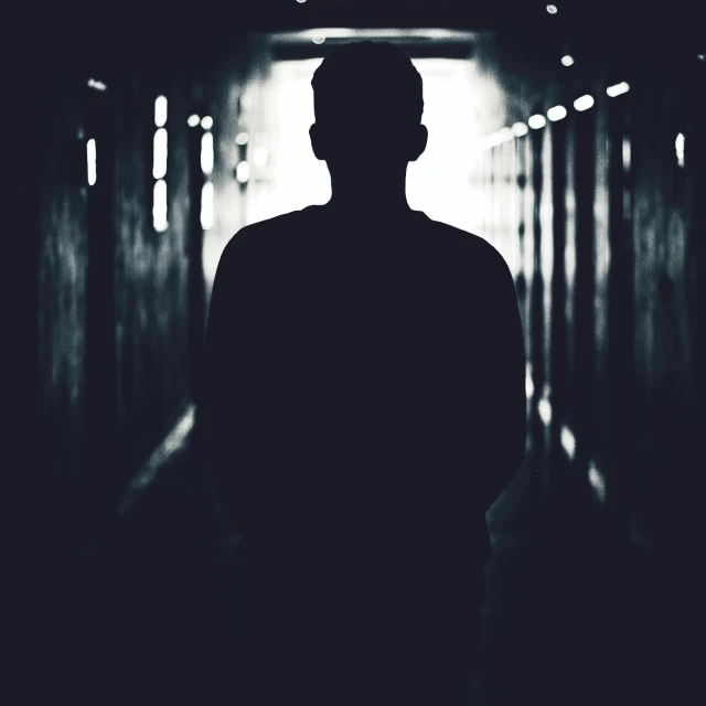 a silhouette of a man standing in a tunnel, a black and white photo, instagram post, dark face, in school hallway, backround dark