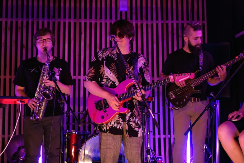 a group of men standing next to each other on a stage, an album cover, by Joe Bowler, pexels, bright glowing instruments, loish |, band playing, non-binary