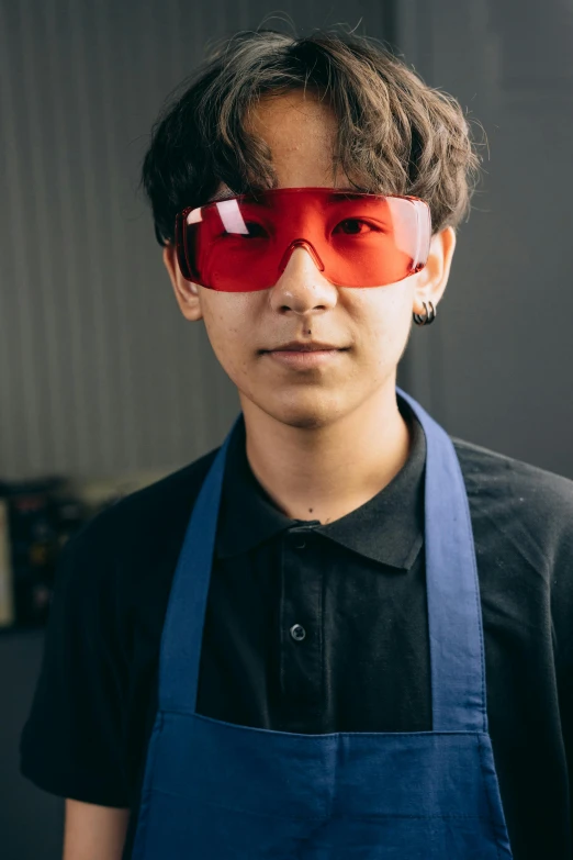 a man wearing a blue apron and red glasses, inspired by Oka Yasutomo, pexels contest winner, altermodern, portrait of 14 years old boy, non binary future world, in a workshop, asian female