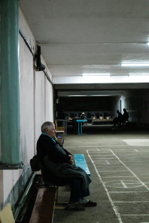 a man sitting on a bench in a parking garage, bengal school of art, typical russian atmosphere, lecture halls and gambling dens, in a row, photograph taken in 2 0 2 0