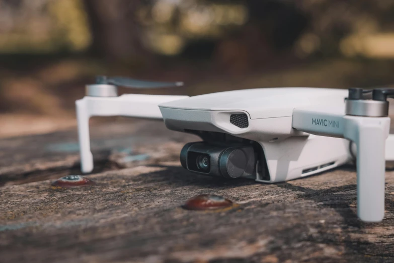 a small white drone sitting on top of a rock, unsplash, ar glasses, high angle security camera feed, on a wooden table, drone speedways