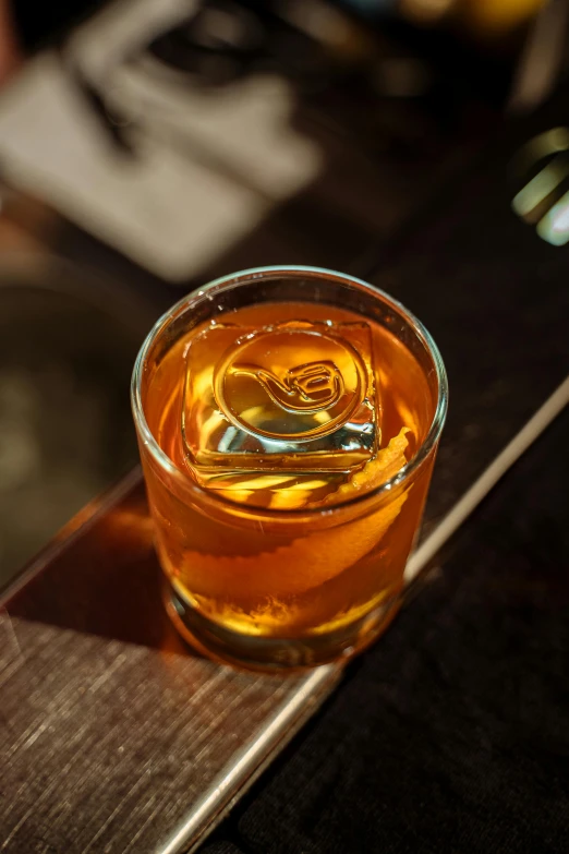 a glass filled with liquid sitting on top of a wooden table, speakeasy, caramel. rugged, zoomed in, spiraling