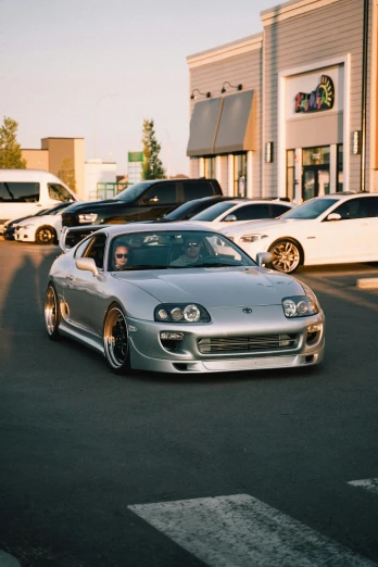 a silver car is parked in a parking lot, unsplash, hyperrealism, toyota supra, ✨🕌🌙, cars and people, modded