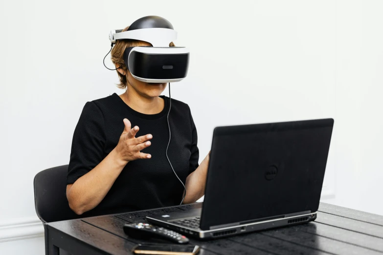 a woman sitting at a table in front of a laptop wearing a virtual reality headset, inspired by Li Di, hurufiyya, whealan, black, third-person view