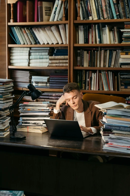 a man sitting at a desk in front of a laptop computer, by Julia Pishtar, trending on pexels, academic art, stacks of books, joe keery, an epic non - binary model, 15081959 21121991 01012000 4k