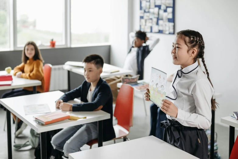 a group of children sitting at desks in a classroom, pexels contest winner, standing sideways, girl wearing uniform, on a canva, commercial