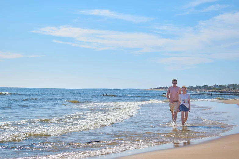 a man and a woman walking along a beach, craigville, clear blue skies, people swimming, family friendly