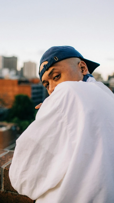 a man sitting on top of a brick wall, an album cover, inspired by Eddie Mendoza, unsplash, lyco art, wearing a navy blue utility cap, bald head, xxxtentacion, shot from roofline