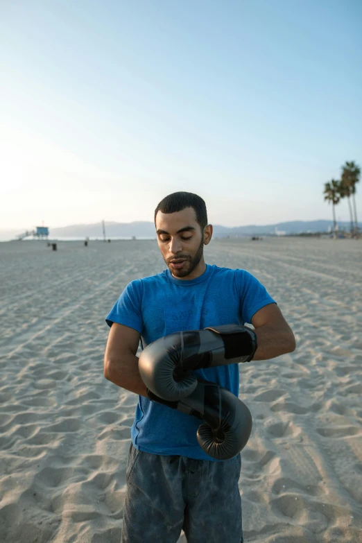 a man holding up his black boxing gloves on a beach