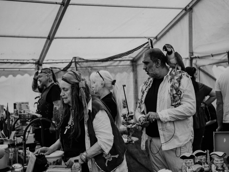 a group of people standing next to each other in a tent, a black and white photo, by Lee Loughridge, unsplash, process art, riding steampunk motorcycle, market stalls, hair worn up, concentration