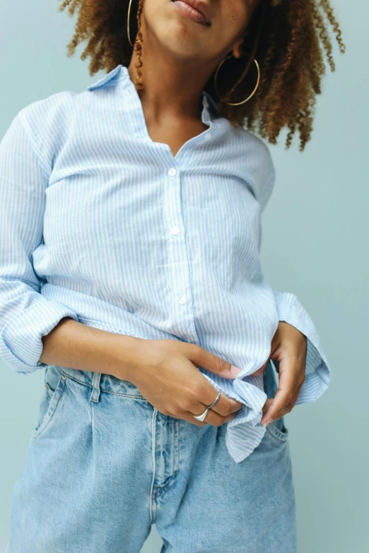 a woman wearing blue and white striped shirt and jeans with big gold hoop earrings